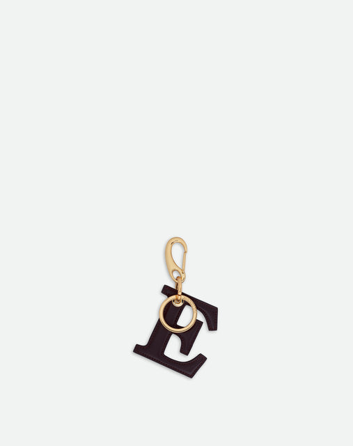 Wandler Bag Charm Letter in the color Grape, deep dark purple, made from brass and lambskin leather with golden hardware, shown on its own against a white background, backside view. 