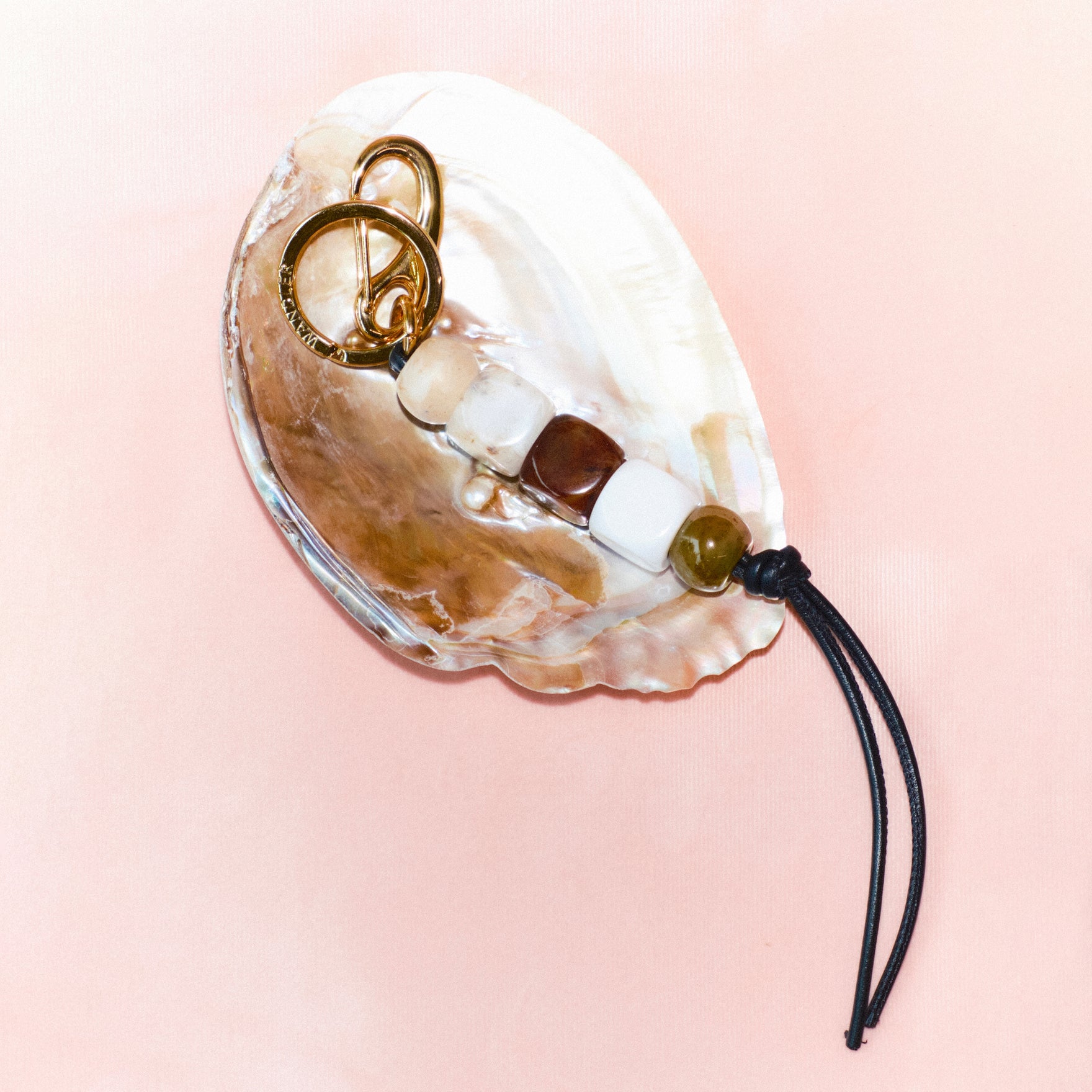 Wandler Bag Charm Marble Mix in brass and lambskin leather with golden hardware, shown as a bag charm, front view, pictured from above, laying on a shell with pink background. 