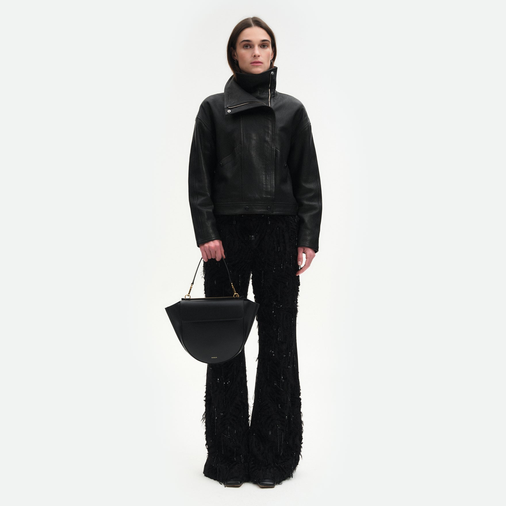 Wandler Hortensia Bag Medium in the color Black, made from Italian calf leather with golden hardware, rounded silhouette and top handle, pictured on model being hand held, full body picture. 