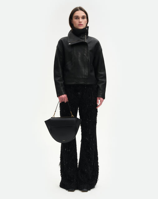 Wandler Hortensia Bag Medium in the color Black, made from Italian calf leather with golden hardware, rounded silhouette and top handle, pictured on model being hand held, full body picture. 