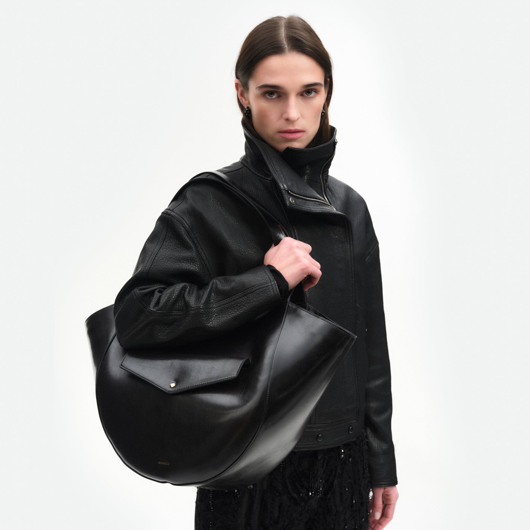 Wandler Hortensia Slouch Tote in the color Black Glaze, made from smooth calf leather with a glaze shine and golden hardware, front view showing clasp closure, pictured being carried on the shoulder by model, half-body picture. 