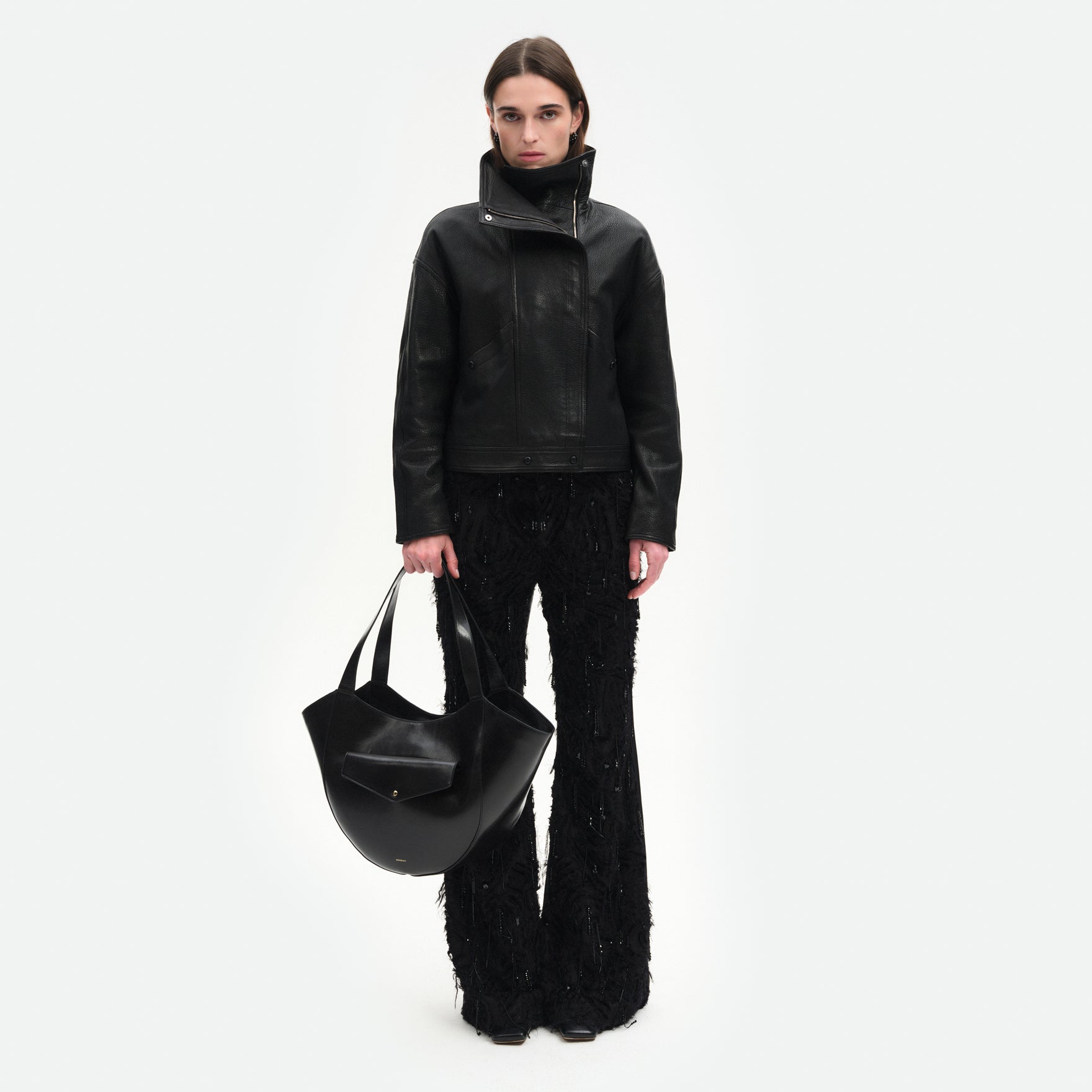 Wandler Hortensia Slouch Tote in the color Black Glaze, made from smooth calf leather with a glaze shine and golden hardware, front view showing clasp closure, pictured being hand-held by model, full body picture. 