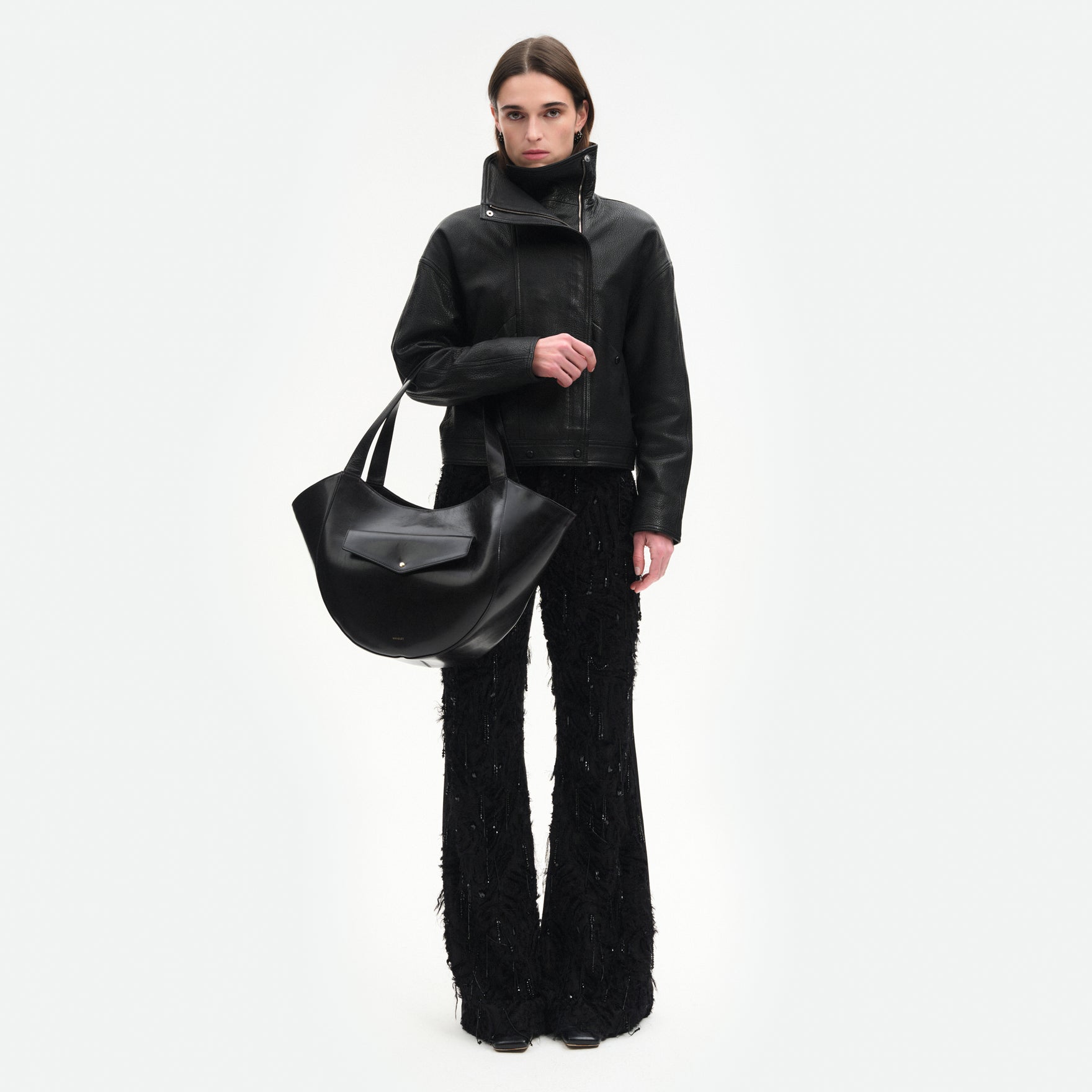 Wandler Hortensia Slouch Tote in the color Black Glaze, made from smooth calf leather with a glaze shine and golden hardware, front view showing clasp closure, pictured being carried on the forearm by model, full body picture. 