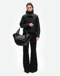 Wandler Hortensia Slouch Tote in the color Black Glaze, made from smooth calf leather with a glaze shine and golden hardware, front view showing clasp closure, pictured being carried on the forearm by model, full body picture. 