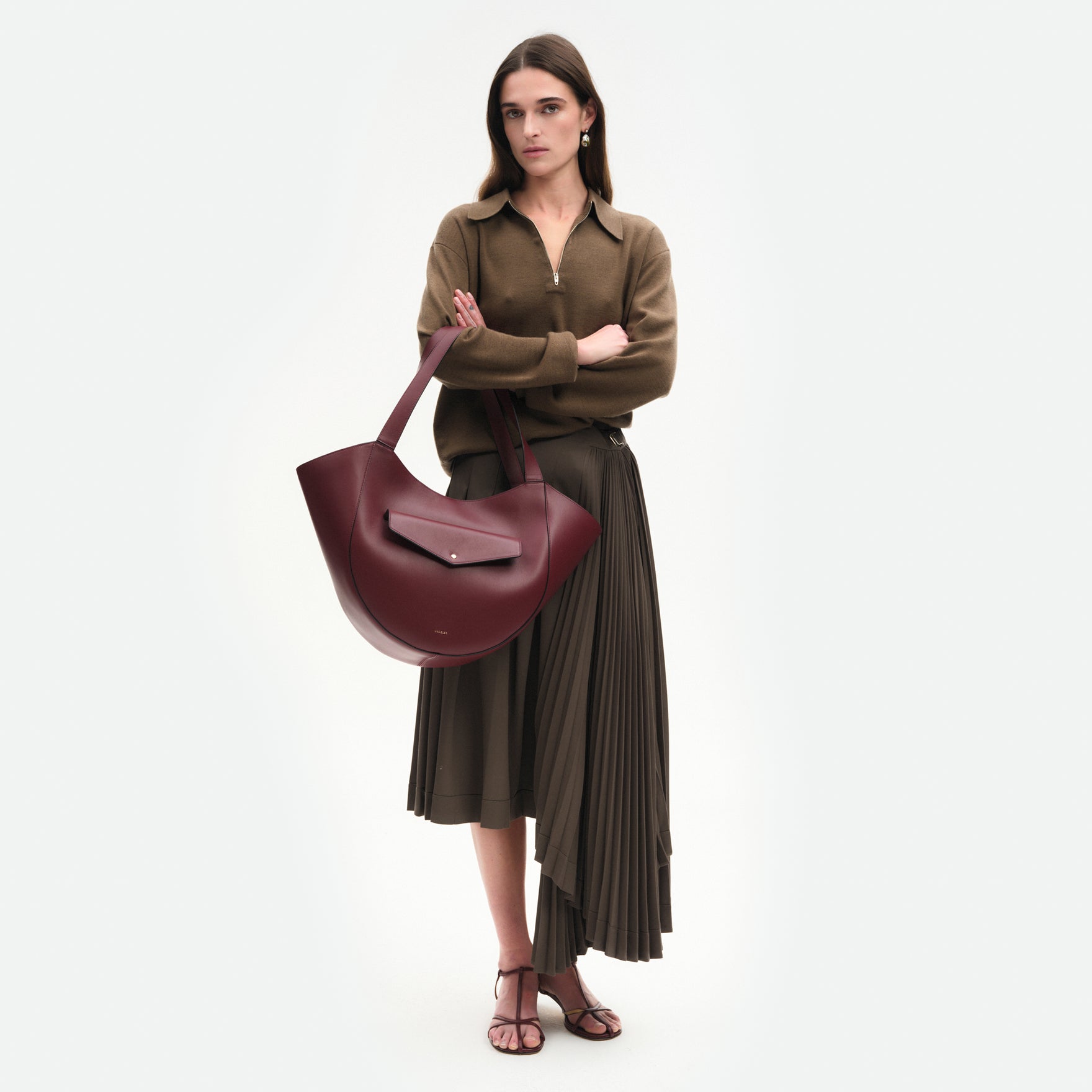 Wandler Hortensia Slouch Tote in the color Bordeaux, deep red made from smooth calf leather with golden hardware, front view showing clasp closure, pictured being carried on the forearm by model, full body picture. 