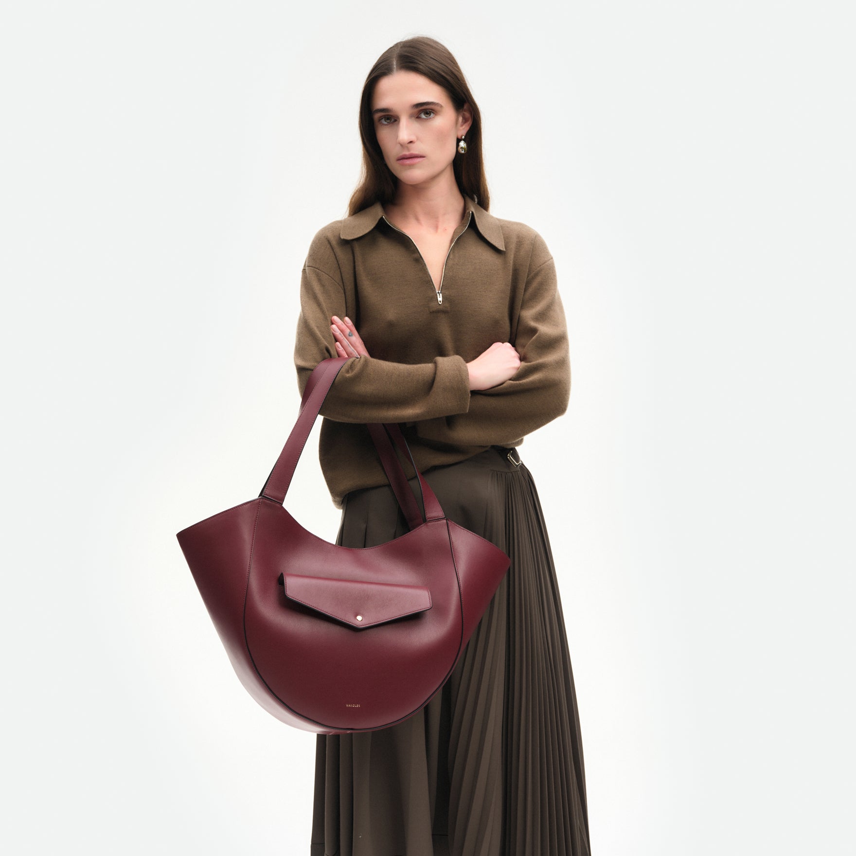 Wandler Hortensia Slouch Tote in the color Bordeaux, deep red made from smooth calf leather with golden hardware, front view showing clasp closure, pictured being carried on the forearm by model, half-body picture. 