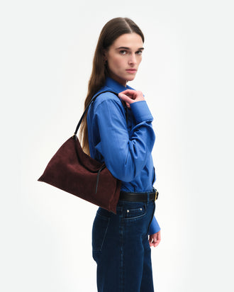 Wandler Penelope Tote Small in the color Acai Suede / Black made from calf leather with golden hardware and soft slouchy silhouette, pictured on model, being worn on the shoulder, half body picture.