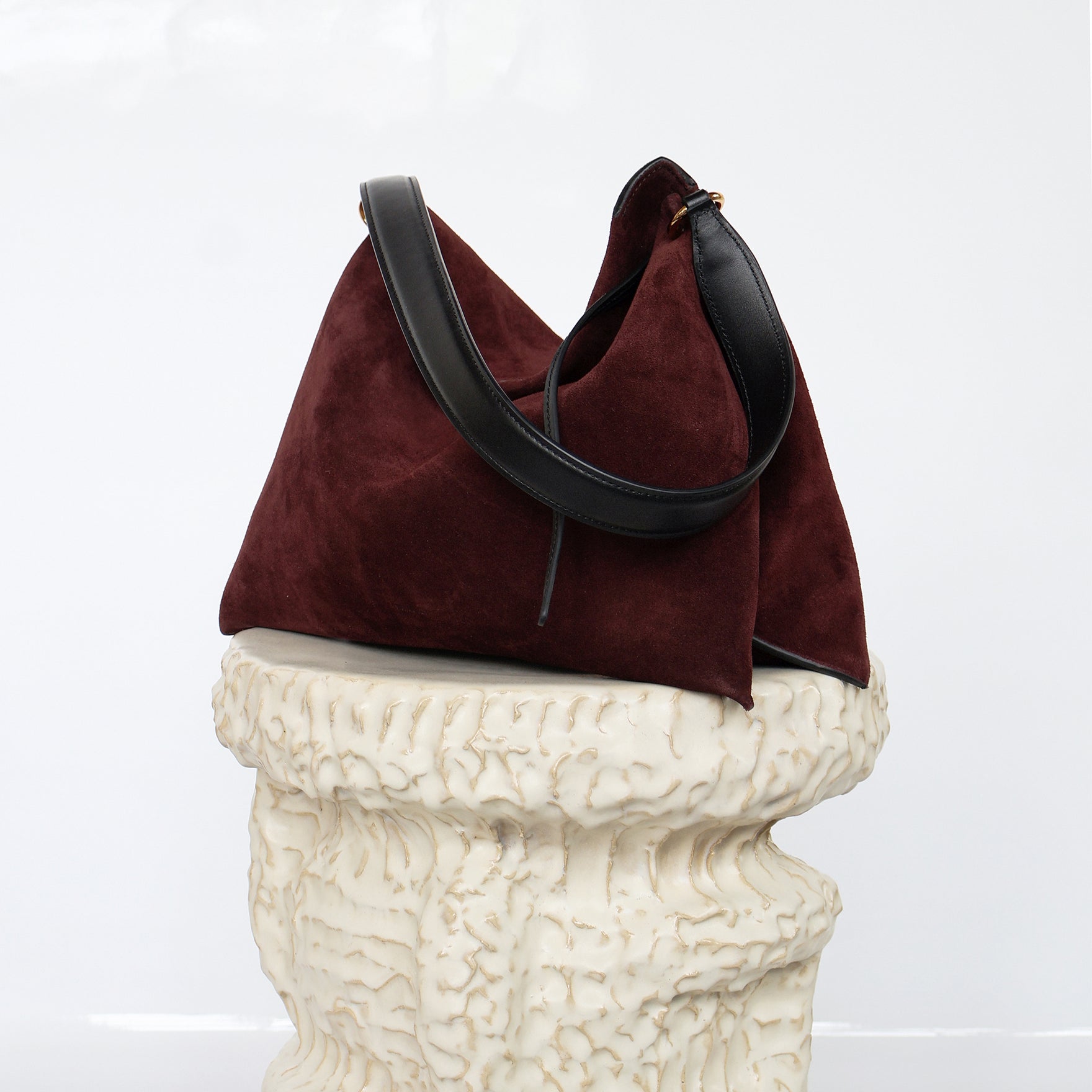 Wandler Penelope Tote Small in the color Acai Suede / Black made from calf leather with golden hardware and soft slouchy silhouette, front view, pictured on pillar.