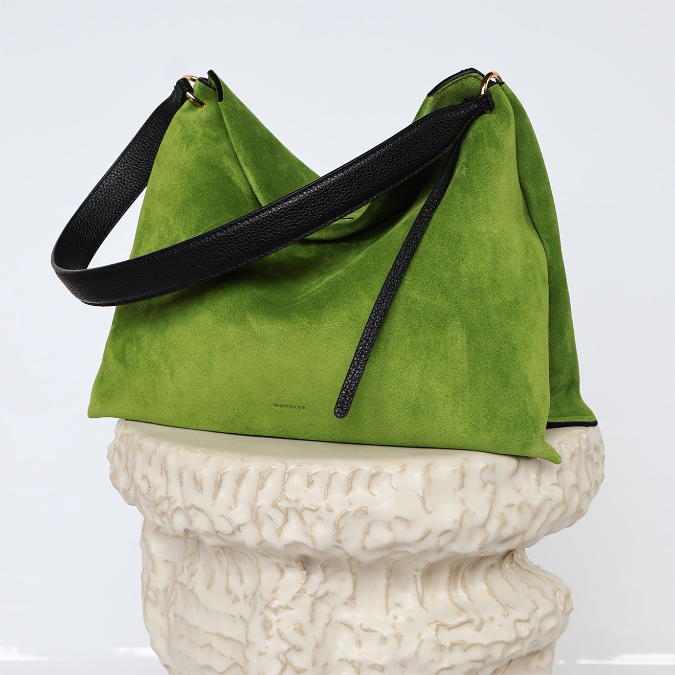 Wandler Penelope Tote Small in the color Verde Suede / Black made from calf leather with golden hardware and soft slouchy silhouette, pictured on pillar.
