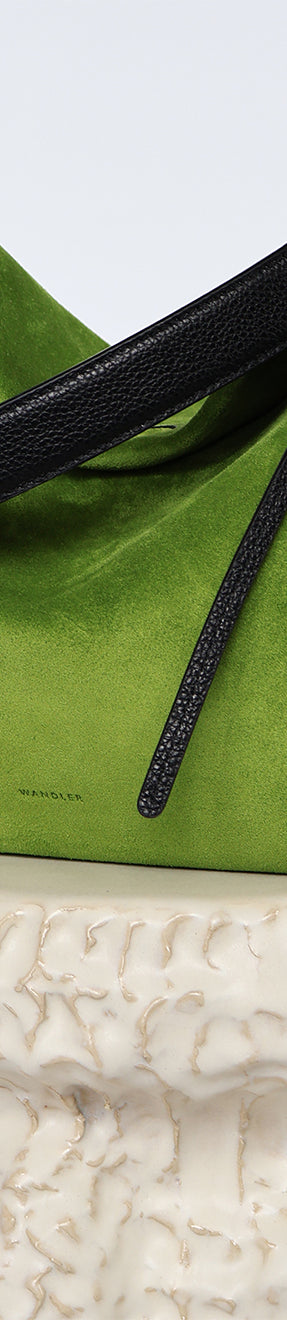 Wandler Penelope Tote Small in the color Verde Suede / Black made from calf leather with golden hardware and soft slouchy silhouette, pictured on pillar.