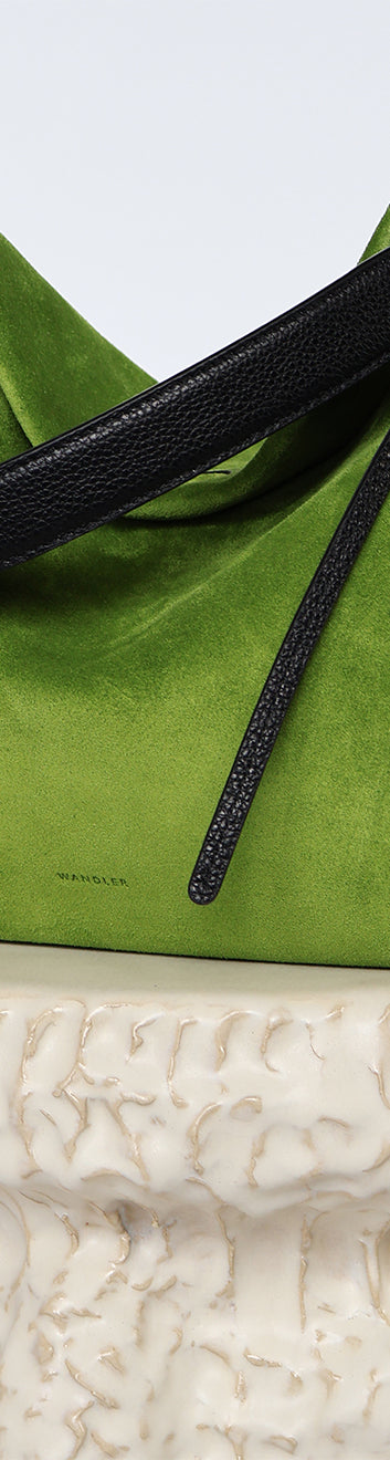 Wandler Penelope Tote Small in the color Verde Suede / Black made from calf leather with golden hardware and soft slouchy silhouette, pictured on pillar.