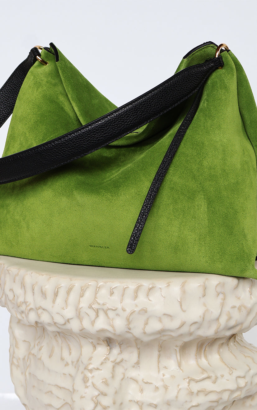 Wandler Penelope Tote Small in the color Verde Suede / Black made from calf leather with golden hardware and soft slouchy silhouette, pictured on pillar.