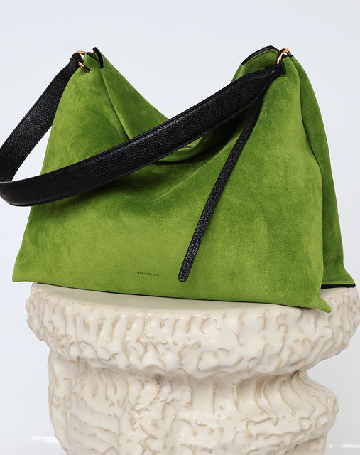 Wandler Penelope Tote Small in the color Verde Suede / Black made from calf leather with golden hardware and soft slouchy silhouette, pictured on pillar.