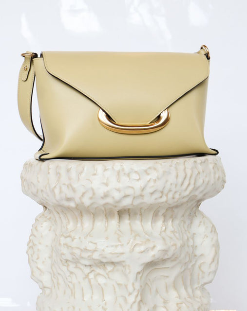Wandler Veneto Shoulder Bag Small in the color Island, made from Italian calf leather with oversized golden clasp hardware, structured silhouette, pictured on pillar.