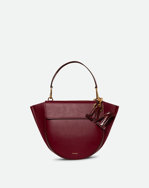 Wandler Bag Charm Letter in the color Bordeaux Python, bordeaux red with python motive, made from brass, lambskin leather with golden hardware, shown attached to a bag, front view.