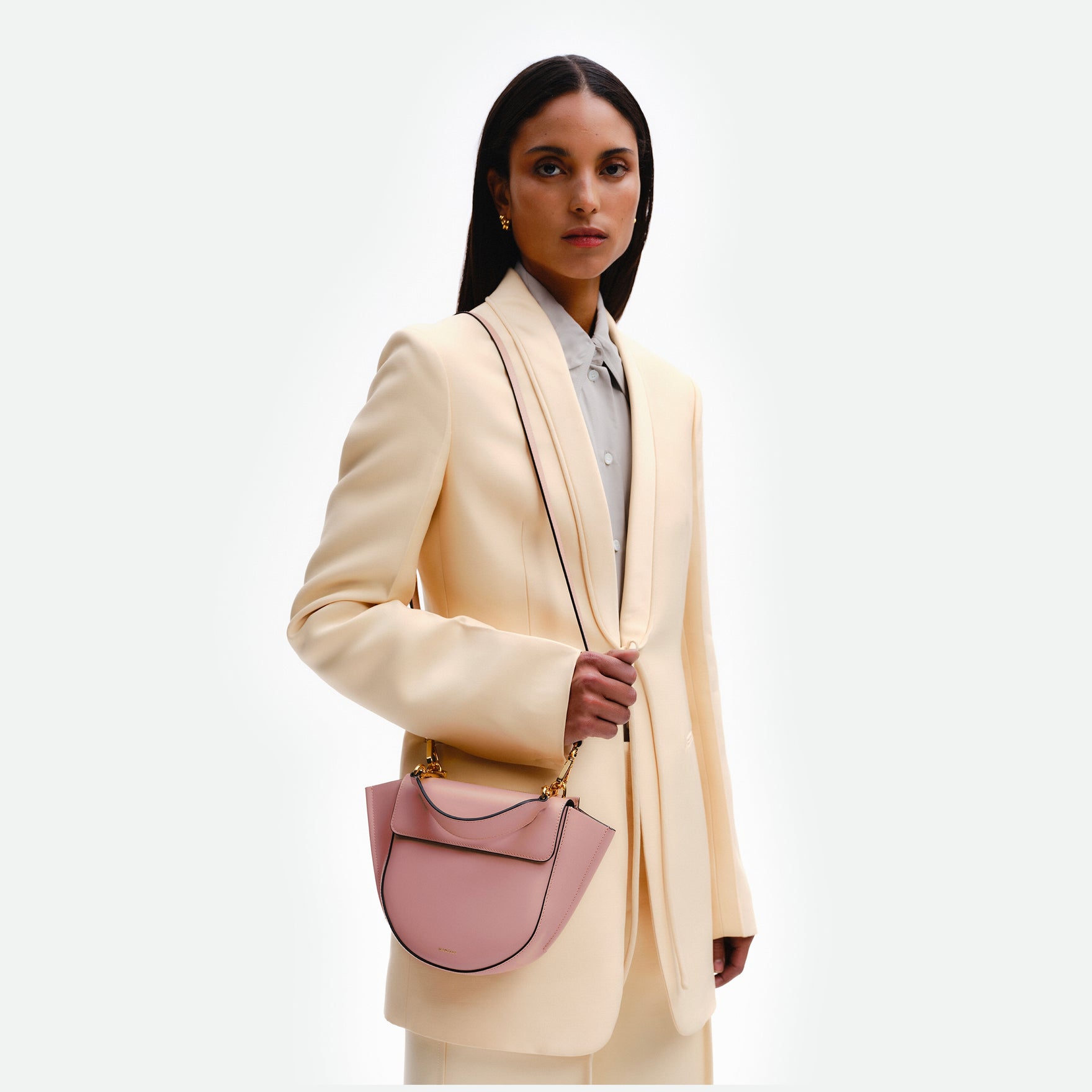 Wandler Hortensia Bag Mini in the color Apricot, light pink, Italian calf leather with golden hardware, rounded silhouette and top handle, pictured on model being worn in a crossbody style. 
