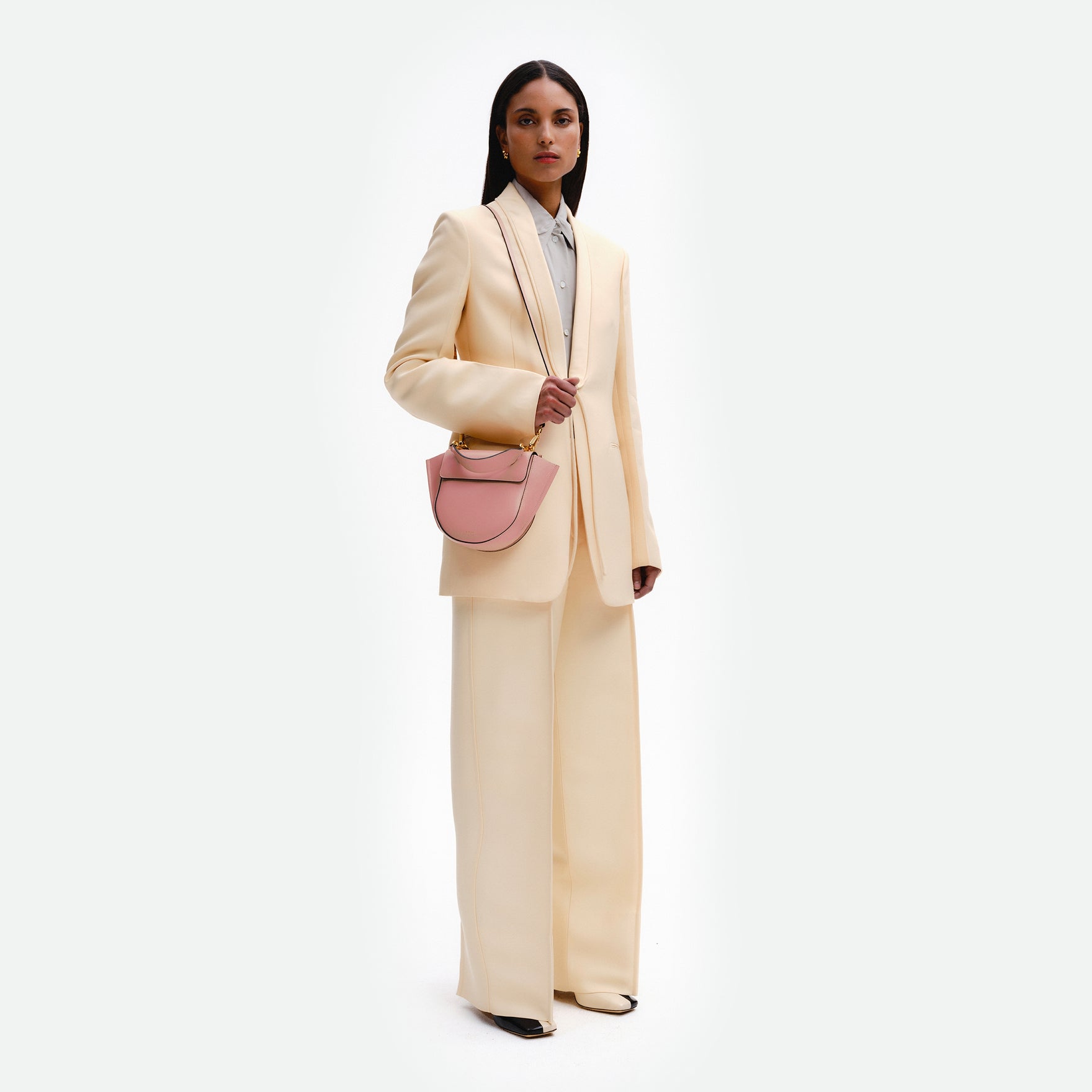Wandler Hortensia Bag Mini in the color Apricot, light pink, Italian calf leather with golden hardware, rounded silhouette and top handle, pictured on model being worn in a crossbody style full body picture.