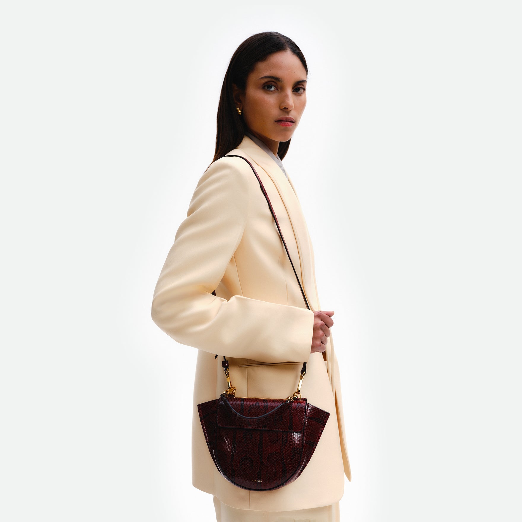 Wandler Hortensia Bag Mini in the color Bordeaux Python, deep dark red with python print, Italian calf leather with golden hardware, rounded silhouette and top handle, pictured being worn on the shoulder on model. 