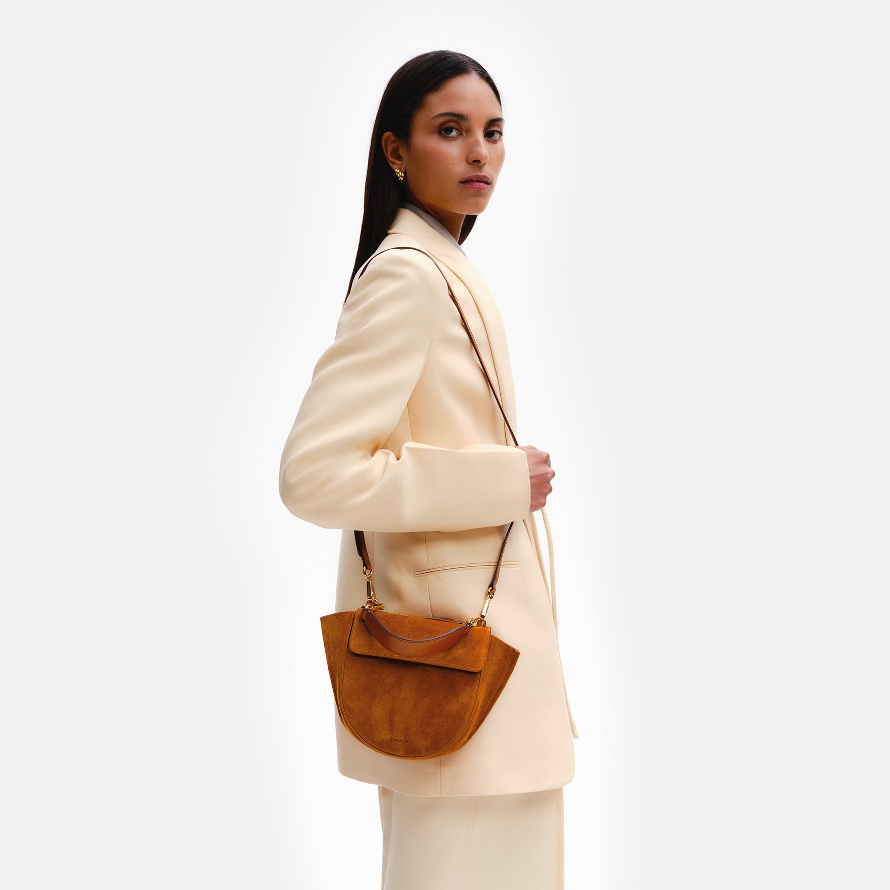 Wandler Hortensia Bag Mini in the color Cognac Suede, soft warm brown suede, Italian calf leather with golden hardware, rounded silhouette and top handle. The bag is pictured on the model, wearing it in the crossbody style.