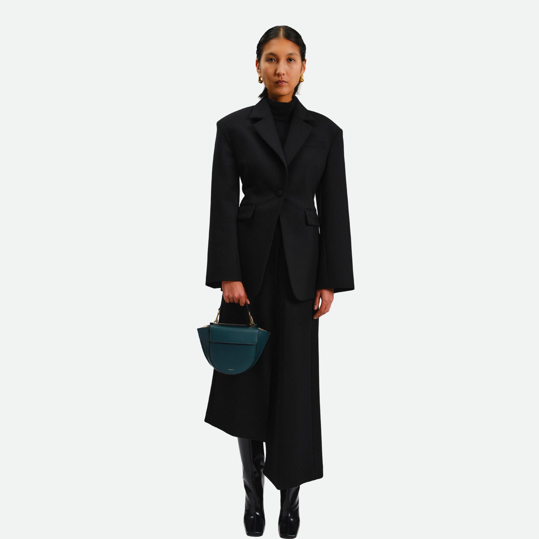 Wandler Hortensia Bag Mini in the color Teal, made from Italian calf leather with golden hardware, rounded silhouette and top handle, pictured being hand held by the model.