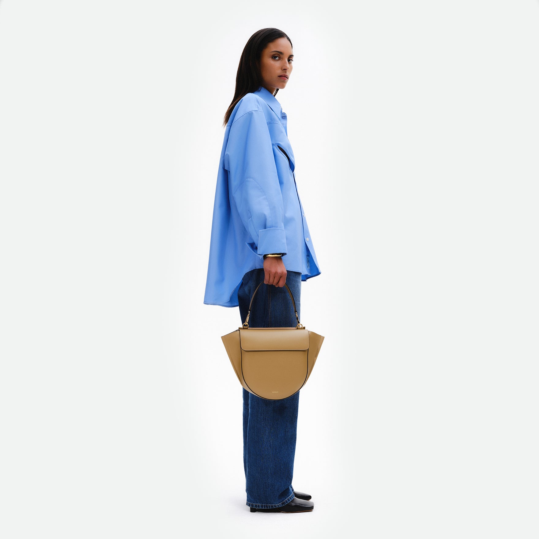 Wandler Hortensia Bag Medium in the color Gingerbread, dark beige, made from Italian calf leather with golden hardware, rounded silhouette and top handle, being hand carried by model. 