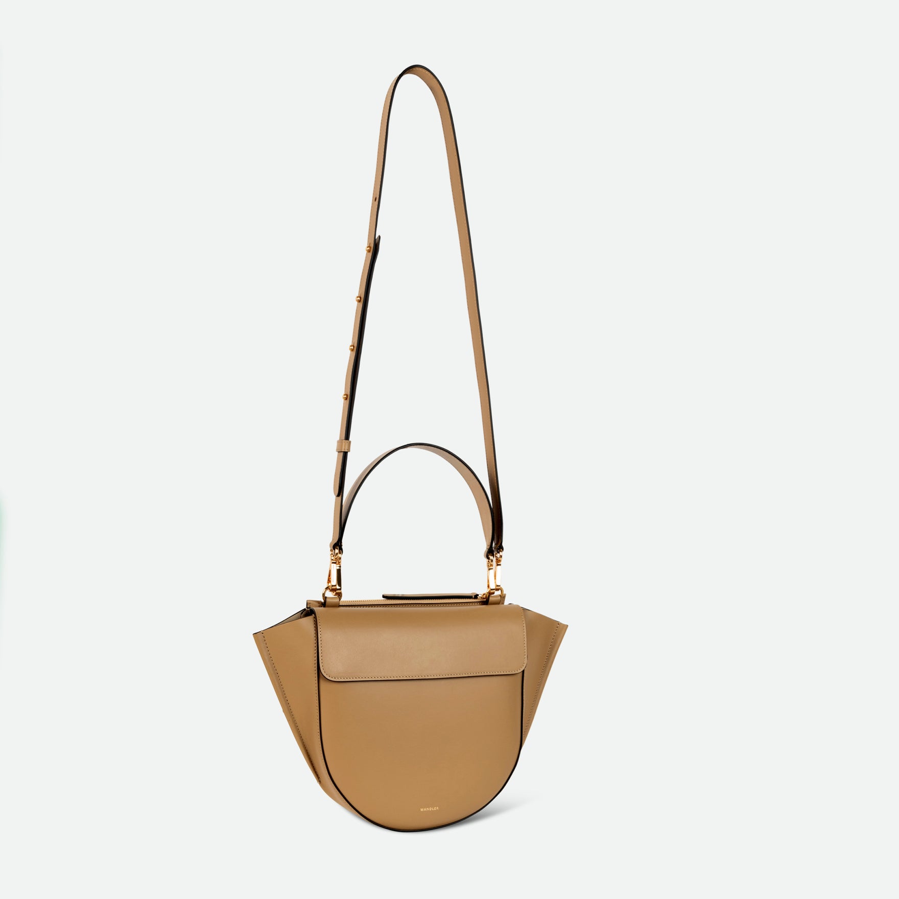 Wandler Hortensia Bag Mini in the color Gingerbread, dark beige, Italian calf leather with golden hardware, rounded silhouette and top handle. The bag is pictured with the crossbody strap extended into the air.