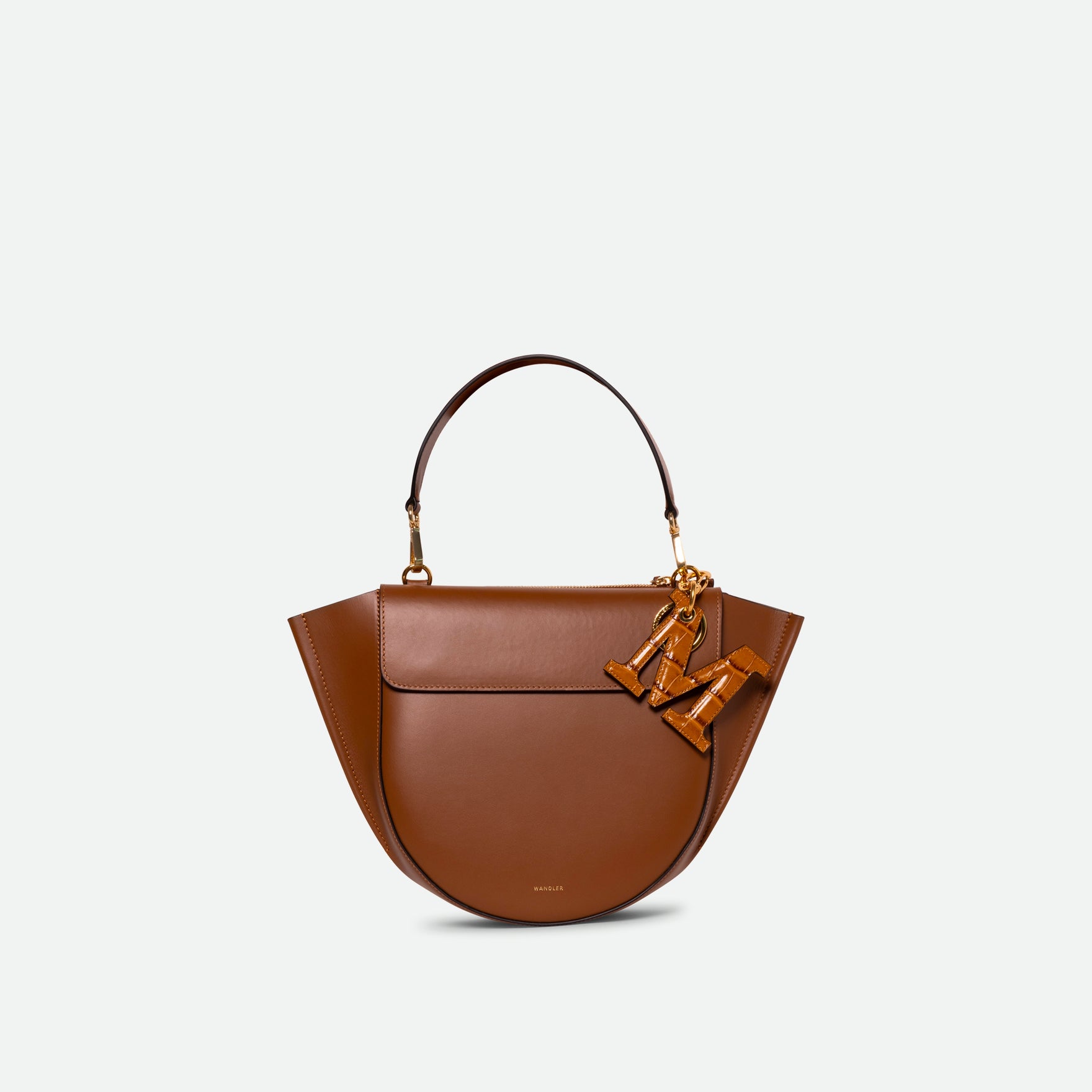 Wandler Bag Charm Letter in the color Saddle Croco, Warm brown with crocodile print, Letter M, made from brass, lambskin leather with golden hardware, pictured being used as a bag charm.