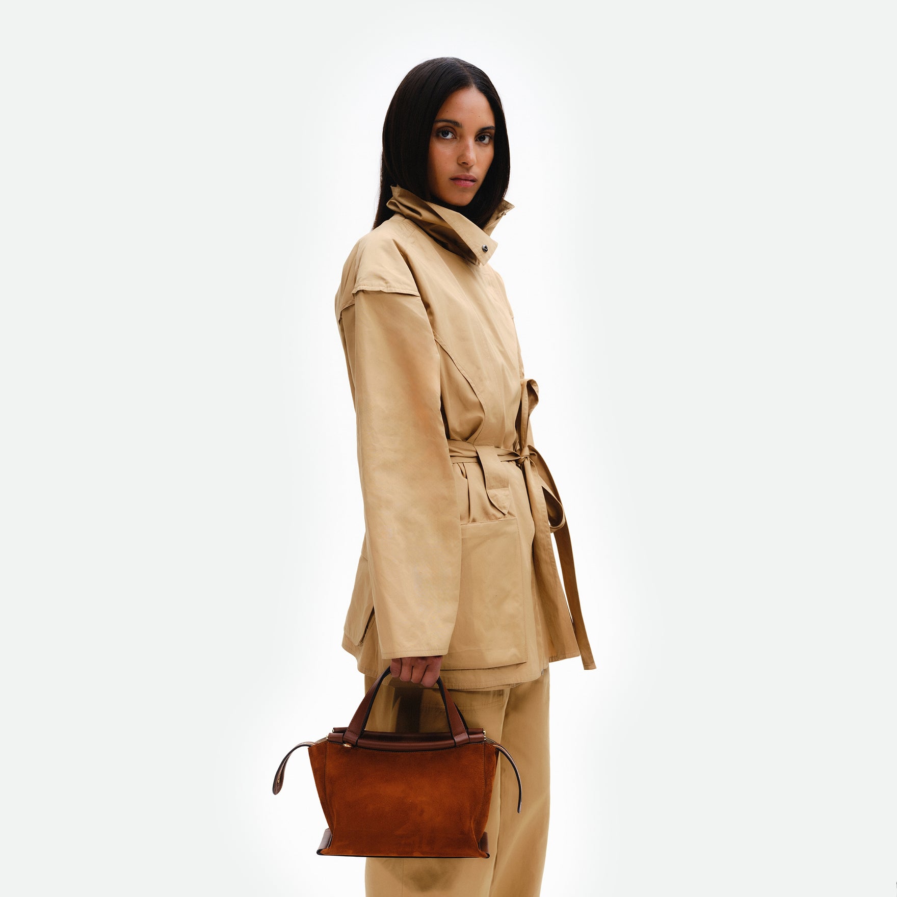 Wandler Ida Bag in the color Tan Suede, made from Italian calf leather with golden hardware and sculptural top handle, pictured being hand held by model.