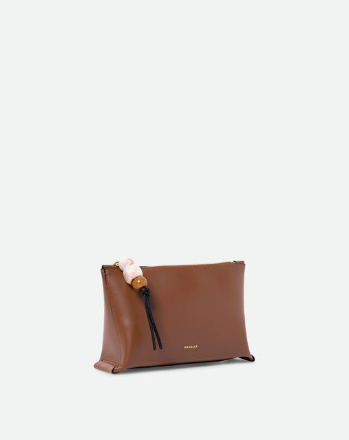 Wandler Ida Case in Saddle, made from calf leather with golden zipper hardware and charm, three quarters view.