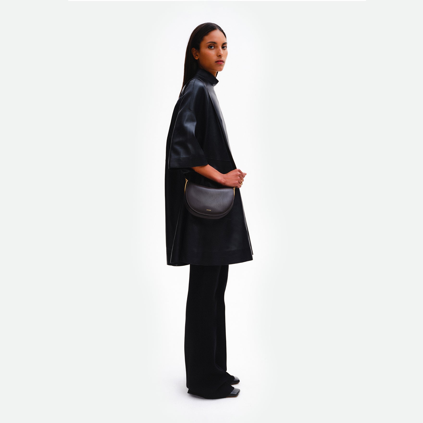 Wandler Kate Bag in the color Black, made from Italian calf leather with golden hardware and adjustable shoulder strap, pictured on model, being worn on the shoulder, full body picture. 