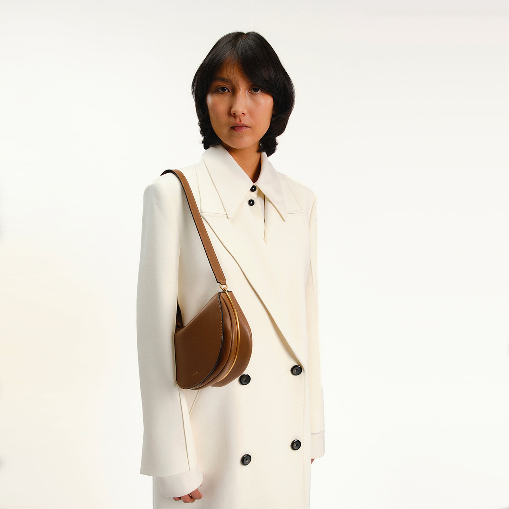 Wandler Kate Saddle Bag in Saddle, made from calf leather with golden hardware and adjustable shoulder strap, worn by model on the shoulder, half body picture.