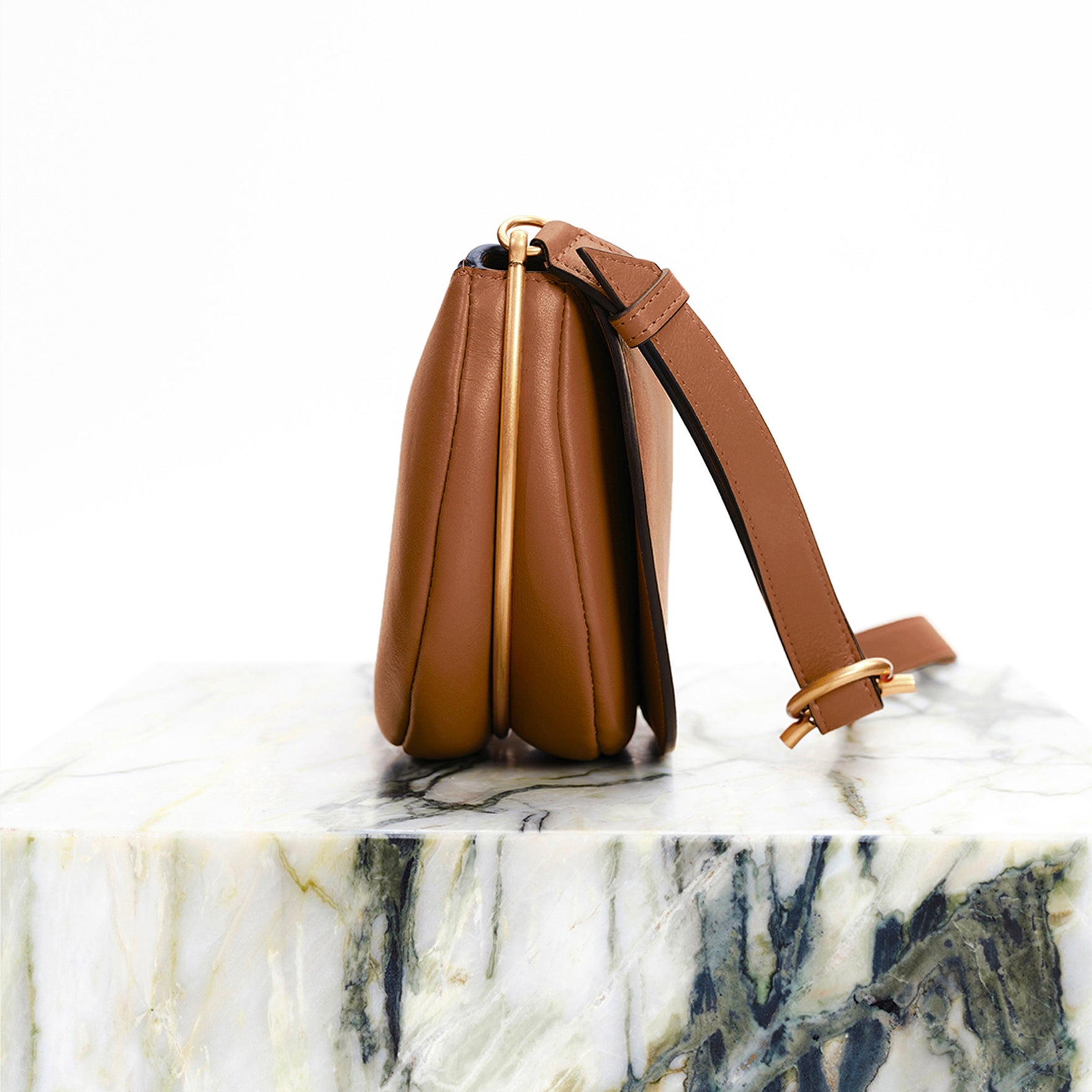Wandler Kate Saddle Bag in Saddle, made from calf leather with golden hardware and adjustable shoulder strap, side view on marble pillar.