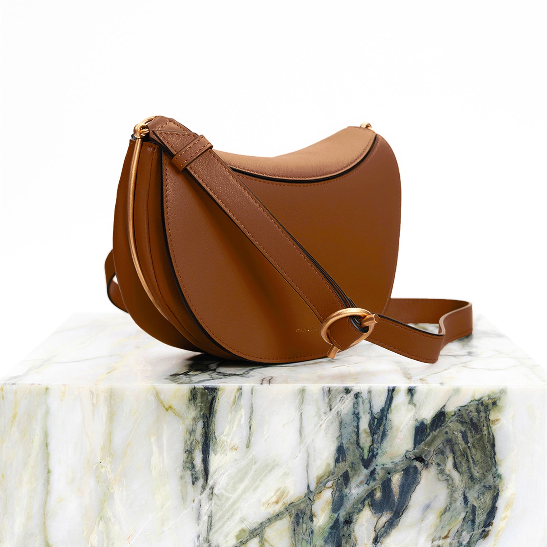 Wandler Kate Saddle Bag in Saddle, made from calf leather with golden hardware and adjustable shoulder strap, photographed on marble pillar.
