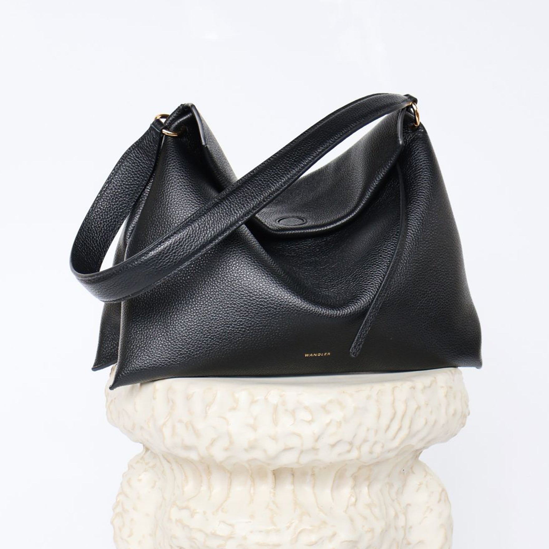 Wandler Penelope Tote Small in the color Black Crust made from calf leather with golden hardware and soft slouchy silhouette, pictured on pillar.