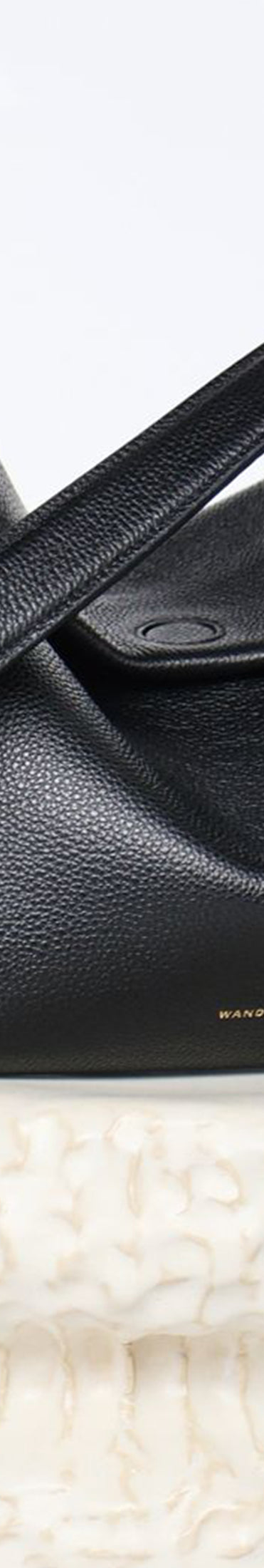Wandler Penelope Tote Small in the color Black Crust made from calf leather with golden hardware and soft slouchy silhouette, pictured on pillar.