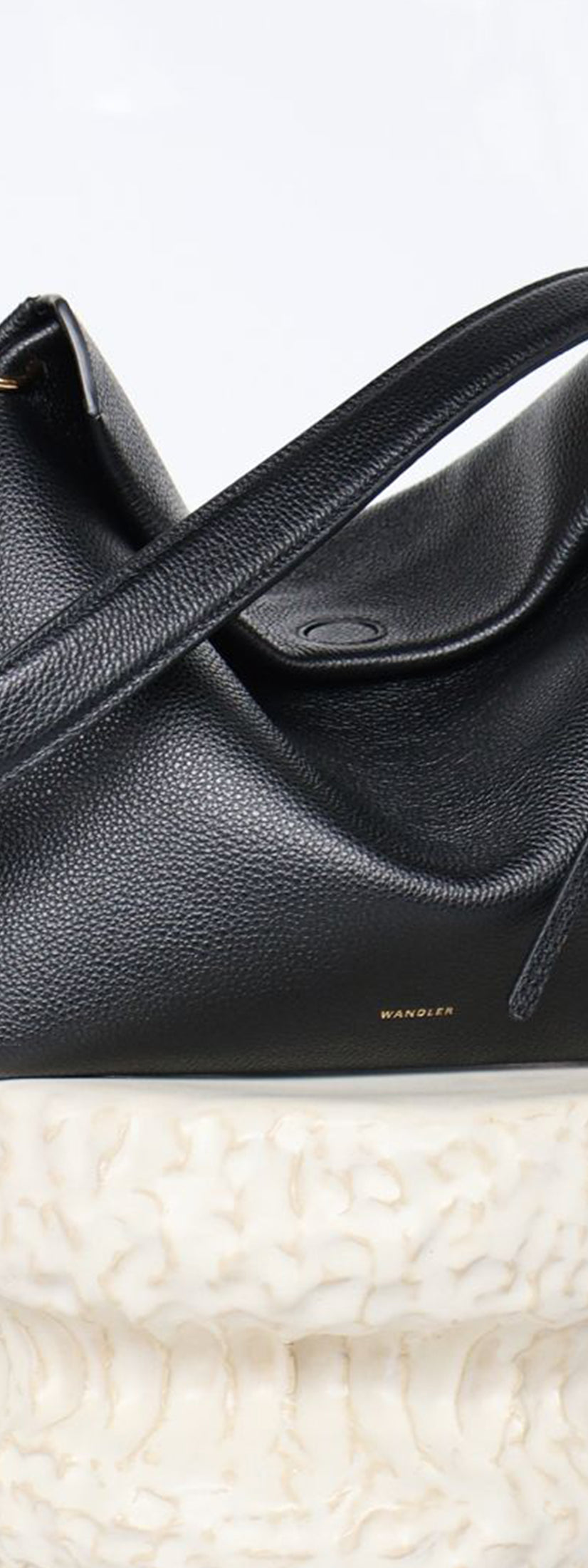 Wandler Penelope Tote Small in the color Black Crust made from calf leather with golden hardware and soft slouchy silhouette, pictured on pillar.