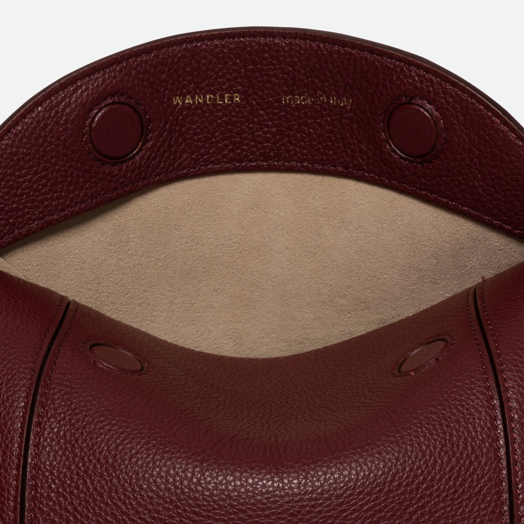 Wandler Penelope Slouch Bag in the color Acai Crust, deep dark red, made from smooth calf leather with golden hardware and adjustable slim strap close up of the leather and buckle with strap. The bag is pictured from the front with the flap open, giving a slight view of the inside of the bag.