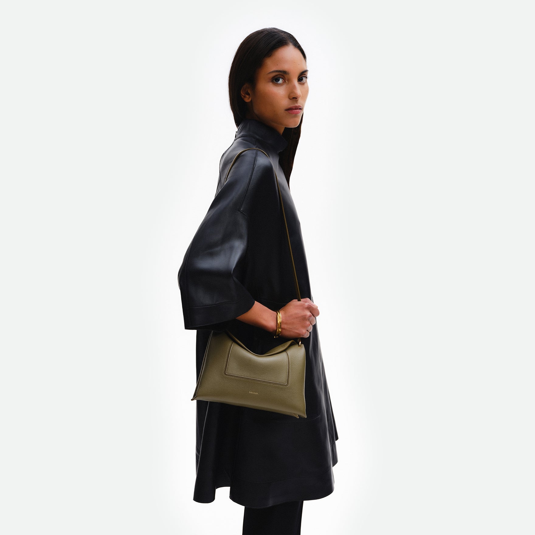 Wandler Penelope Slouch Bag in the color Olive Crust, green, made from smooth calf leather with golden hardware and adjustable slim strap. The bag is pictured being worn on the shoulder by model.