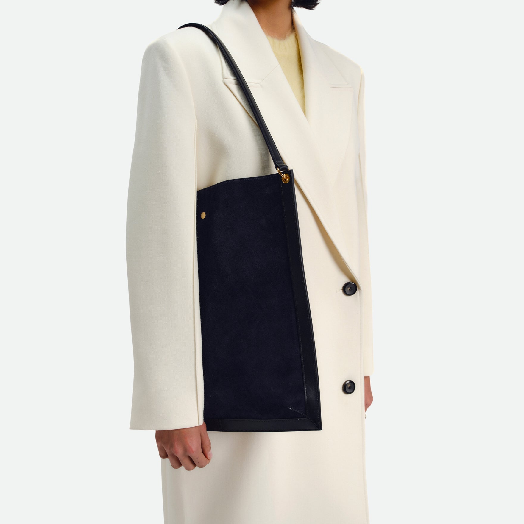 Wandler Penny Tote in the color Black Suede, made from Italian calf leather with hand-painted black edges and golden hardware, close up of the bag being worn on the shoulder by model.