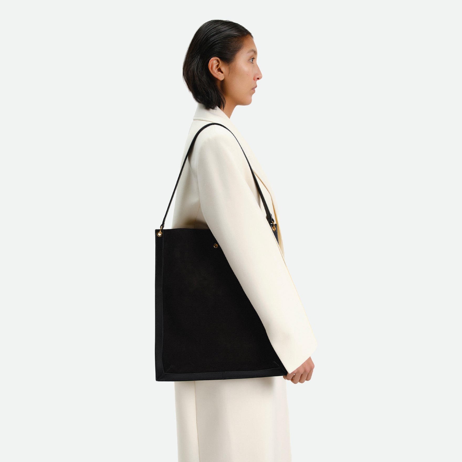 Wandler Penny Tote in the color Black Suede, made from Italian calf leather with hand-painted black edges and golden hardware, being worn by the model on the shoulder.