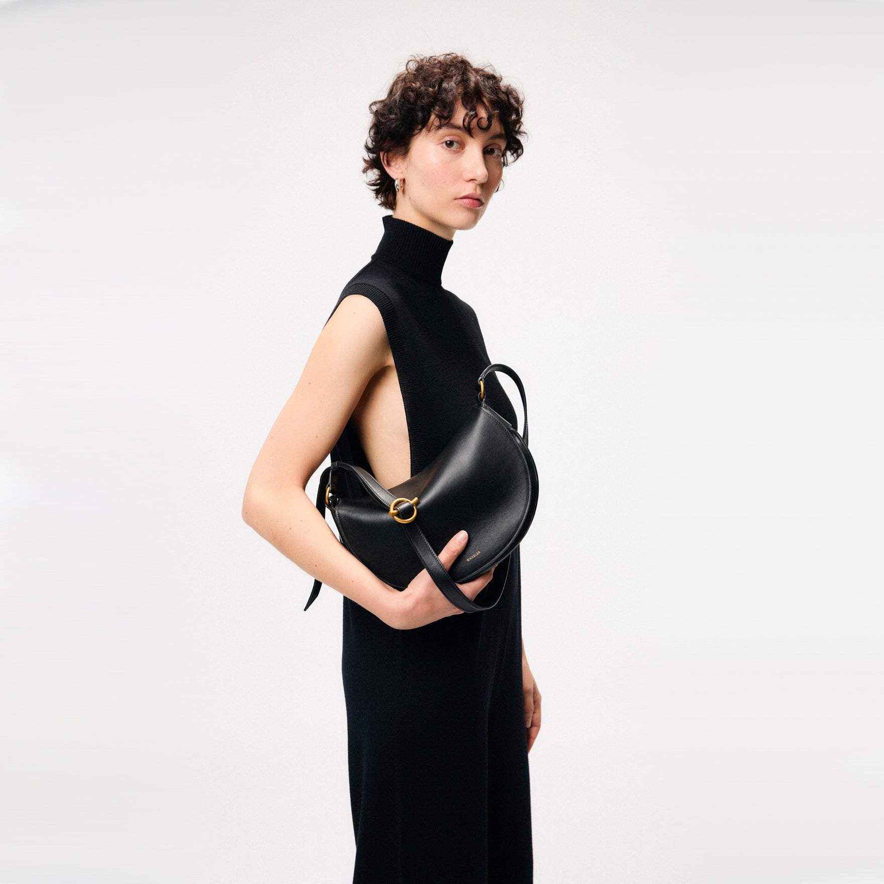 Wandler Kate Bag Big in the color Black, made from Italian calf leather with golden hardware and adjustable shoulder strap, pictured being held in the hand by model, half body picture.