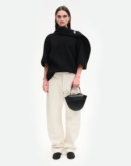 Wandler Hortensia Bag Mini in the color black, Italian calf leather with golden hardware, rounded silhouette and top handle, pictured being hand-held by model. 