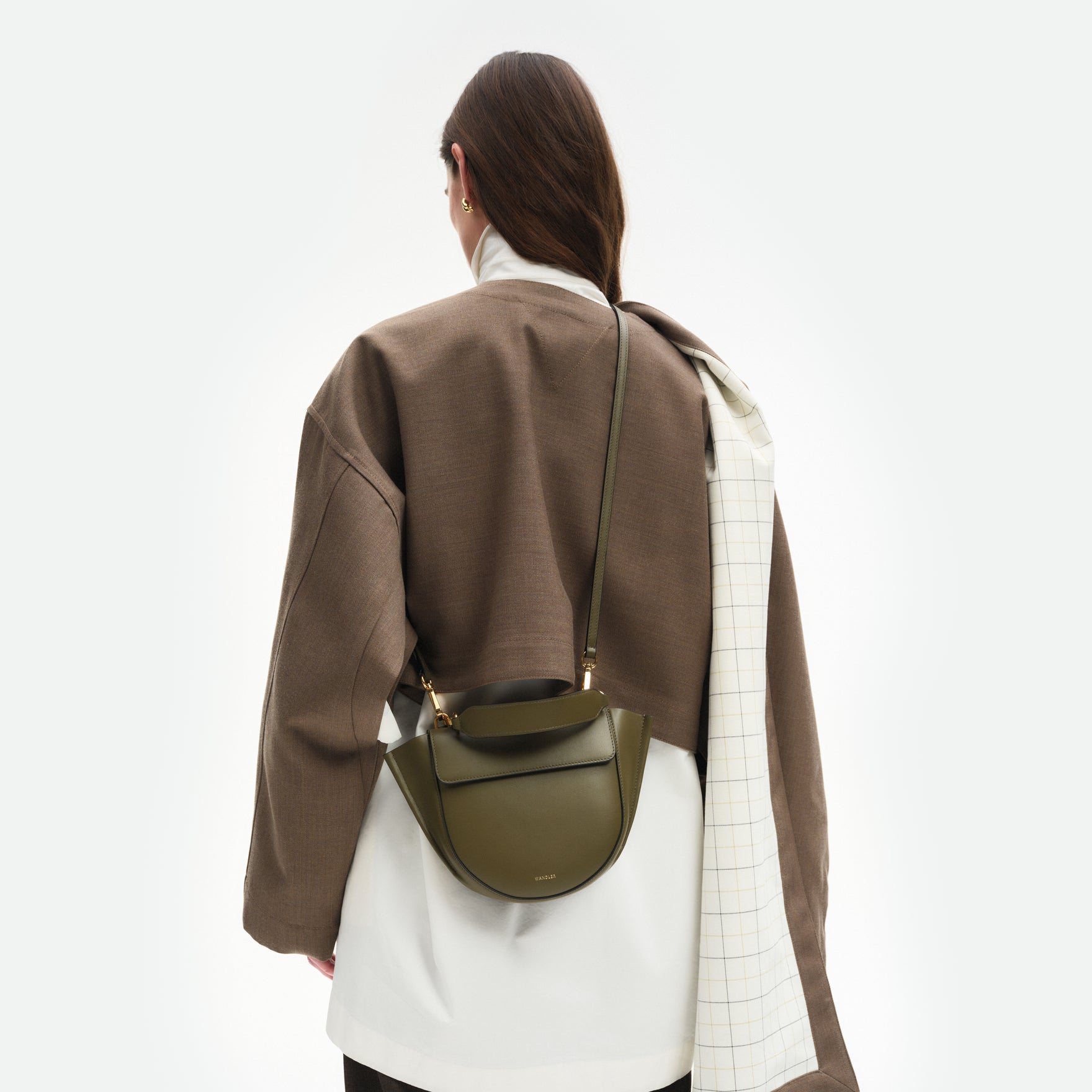 Wandler Hortensia Bag Mini in the color Deep Olive, Olive green, made from Italian calf leather with golden hardware, rounded silhouette and top handle, pictured on model, worn in crossbody style, half body picture. 