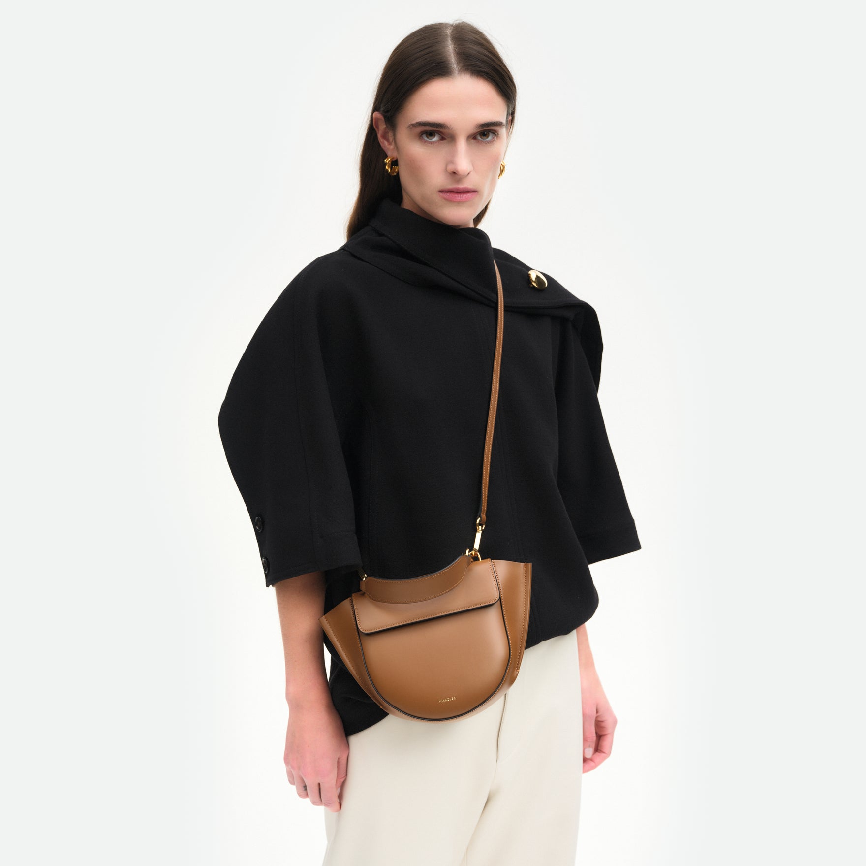 Wandler Hortensia Bag Mini in the color Saddle, brown, Italian calf leather with golden hardware, rounded silhouette and top handle. Bag is pictured being worn by model in crossbody style front view.
