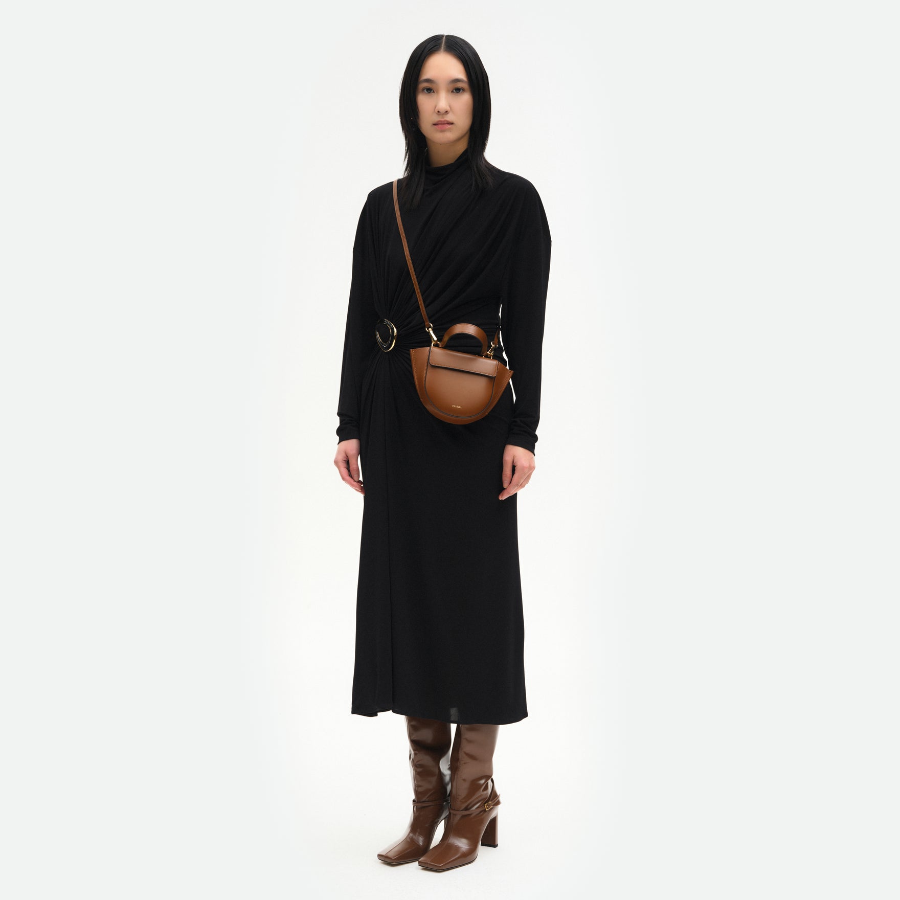 Wandler Hortensia Bag Piccola in the color Saddle, warm brown, made from Italian calf leather with golden hardware and rounded silhouette. Bag is pictured being worn by the model in a crossbody style, full body picture.