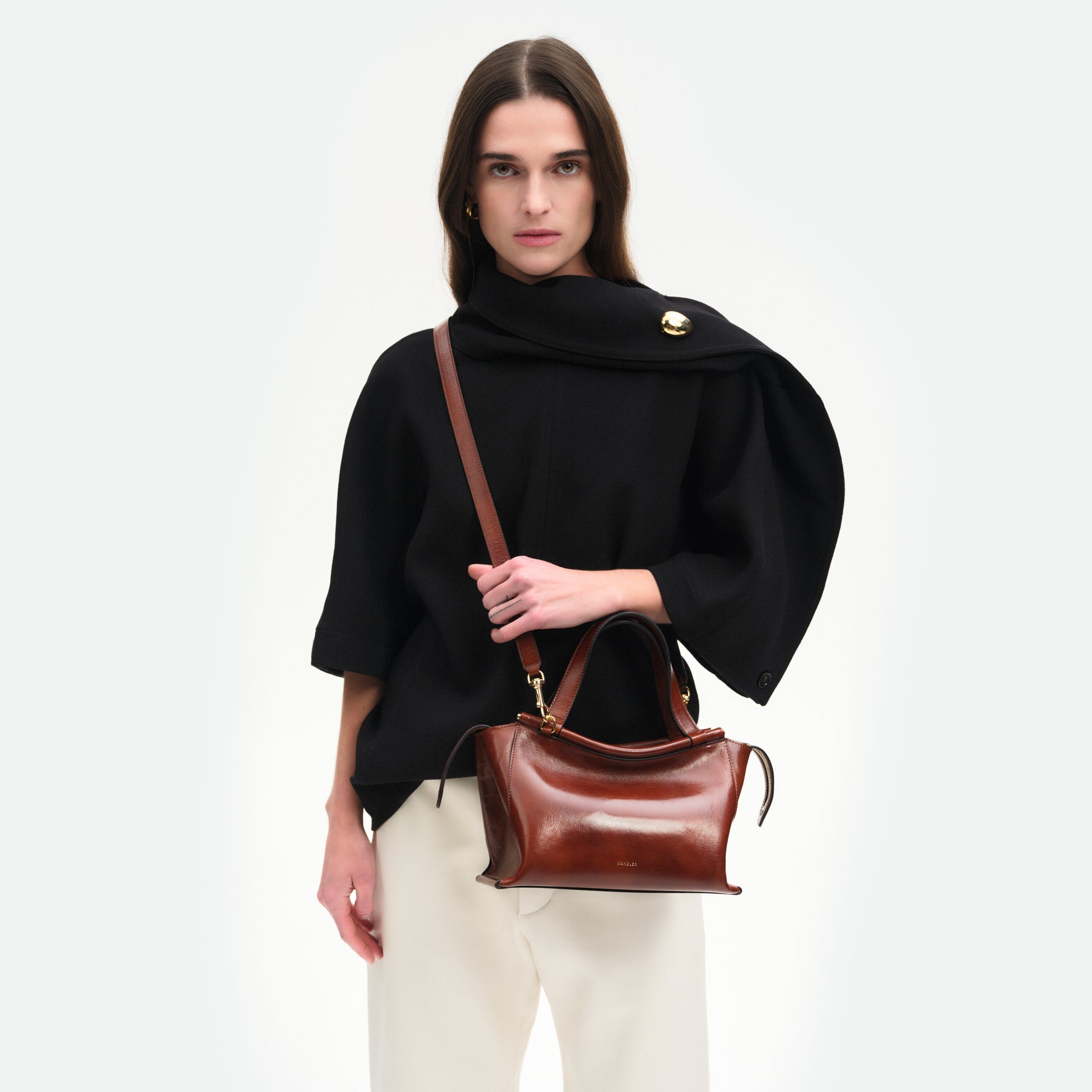 Wandler Ida Bag in the color Palissander Glaze, deep dark brown with red undertones, made from Italian calf leather with golden hardware and sculptural top handle, pictured on model, worn in a crossbody style. 