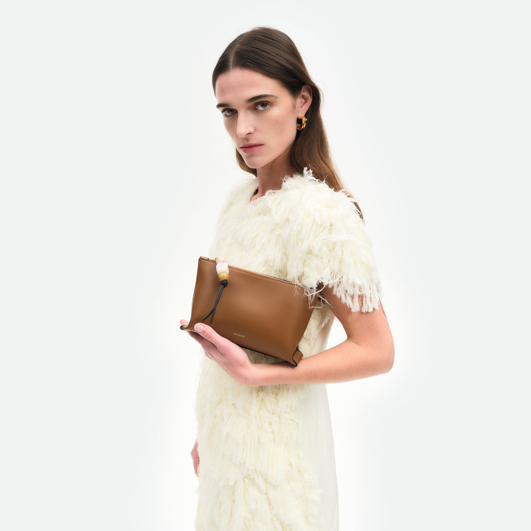 Wandler Ida Case in Saddle, made from calf leather with golden zipper hardware and charm, pictured being held in the hand by model.