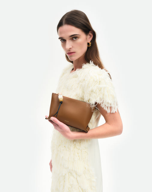 Wandler Ida Case in Saddle, made from calf leather with golden zipper hardware and charm, pictured being held in the hand by model.
