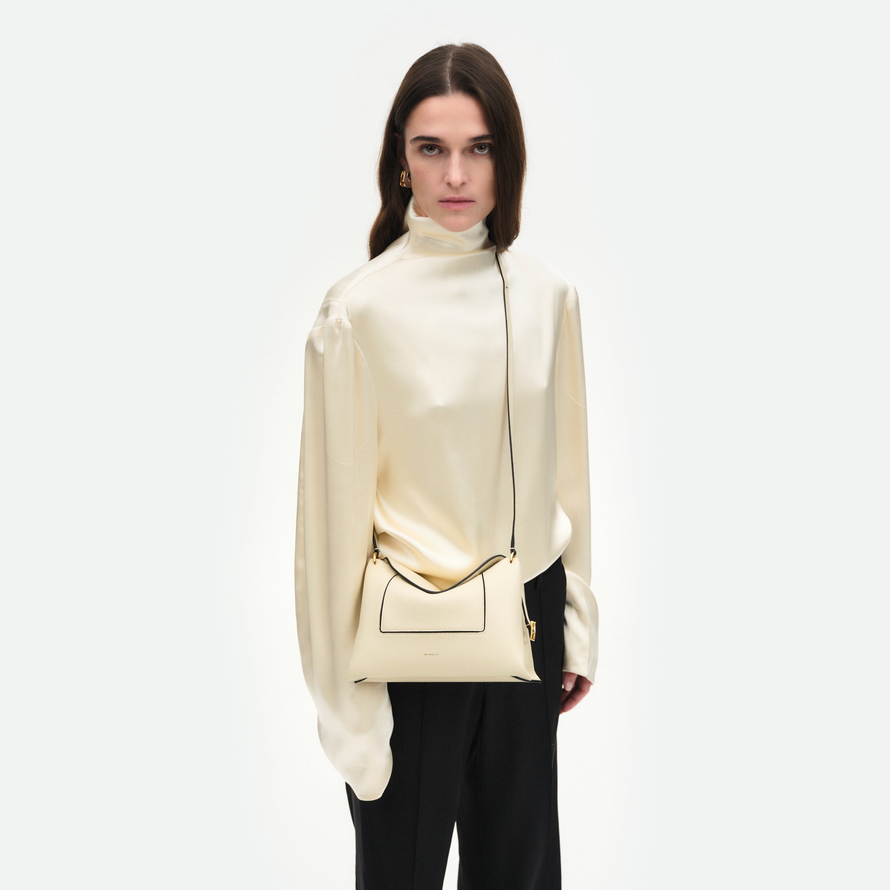 Wandler Penelope Slouch Bag in the colour Beige Crust, beige, made from smooth calf leather with golden hardware and adjustable slim strap, pictured on model, worn as a crossbody bag, front view.