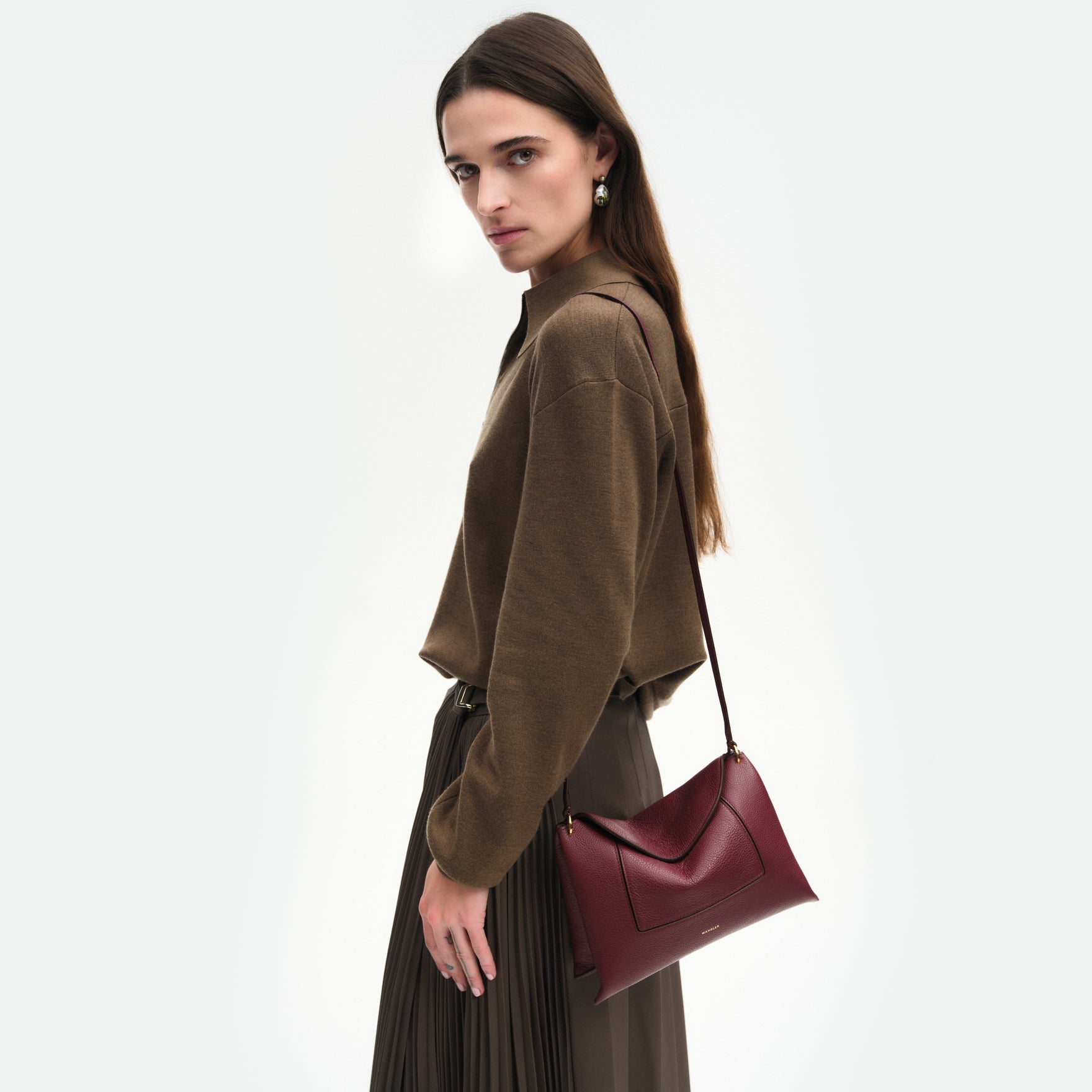 Wandler Penelope Slouch Bag in the color Acai Crust, deep dark red, made from smooth calf leather with golden hardware and adjustable slim strap close up of the leather and buckle with strap, shown on model, worn on the shoulder. 